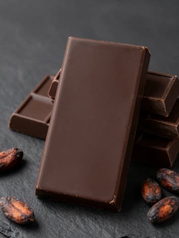 Stacked dark chocolate blocks on black slate with scattered cacao beans
